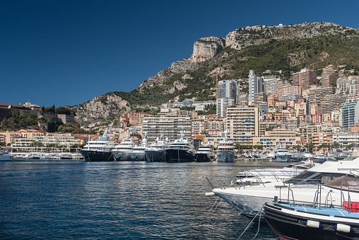 Luxury yachts berthed in the Port Hercules harbour of  Monaco Monte Carlo. In the background overlooking the harbour is the Rock of Monaco where  the Prince's Palace can be seen, together with the many high rise luxury apartment buildings climbing the hillside