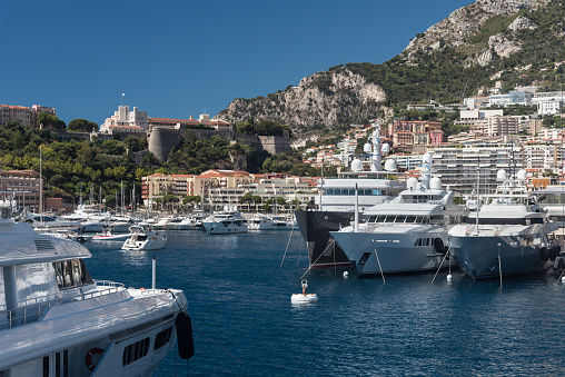 Luxury yachts berthed in the Port Hercules harbour of  Monaco Monte Carlo. In the background overlooking the harbour is the Rock of Monaco where Monaco-Ville, the oldest part of Monaco, and the Prince's Palace can be seen, together with the many high rise luxury apartment buildings climbing the hillside