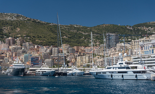 Luxury yachts berthed in the Port Hercules harbour of  Monaco Monte Carlo. In the background overlooking the harbour are the many high rise luxury apartment buildings climbing the hillside