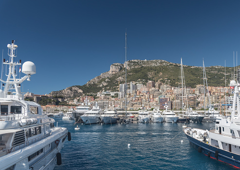 Luxury yachts berthed in the Port Hercules harbour of  Monaco Monte Carlo. In the background overlooking the harbour are the many high rise luxury apartment buildings climbing the hillside