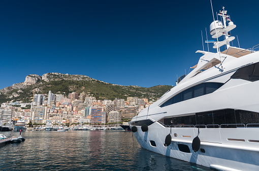 Luxury yachts berthed in the Port Hercules harbour of  Monaco Monte Carlo. In the background overlooking the harbour are the many high rise luxury apartment buildings climbing the hillside
