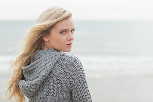 Close up portrait of a cute young woman in gray knitted jacket on the beach
