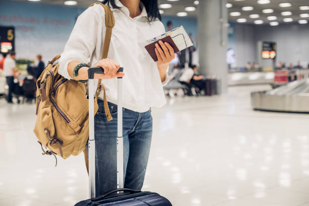Woman backpacker holding passport and map with suitcase standing at check in baggage at airport terminal,traveler concept stock photo