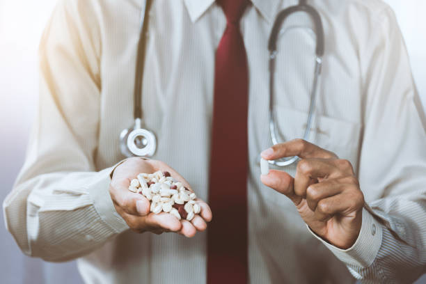 asian male doctor displaying a handful of pills in his palm - vitamin pill picking up pill capsule imagens e fotografias de stock