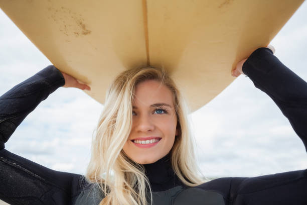 istock Smiling woman in wet suit holding surfboard over head 841063896