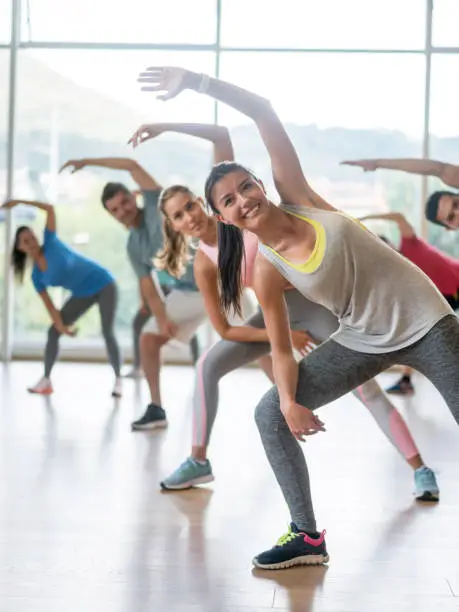 Group of Latin American people in an aerobics class at the gym stretching and looking very happy - healthy concepts