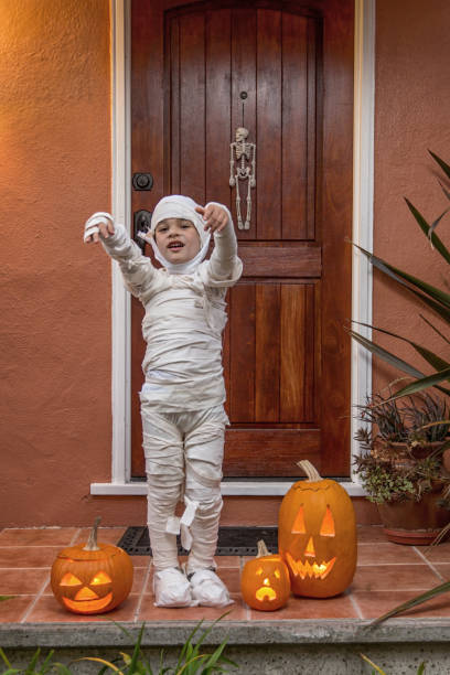 Happy 5 year old wearing a handmade mummy costume, trick or treating in a neighborhood
