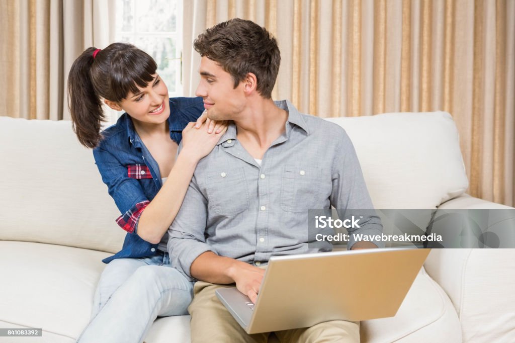 Young couple using a laptop Young couple using a laptop while sitting on a sofa in a living room 18-19 Years Stock Photo