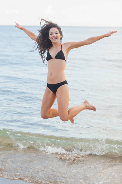 istock Cheerful young woman in bikini jumping at beach 841083774