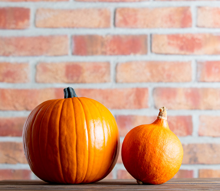 Two Autumn pumpkins on wooden table with brick wall at background