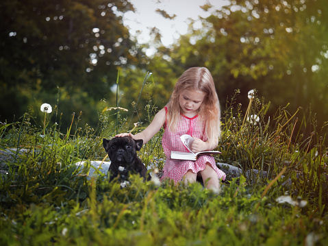 Girl with dog reading a book in nature