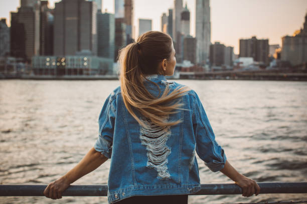 This city is breathtaking Rear view shot of woman standing in front of New York skyline with her arms outstretched denim jacket stock pictures, royalty-free photos & images