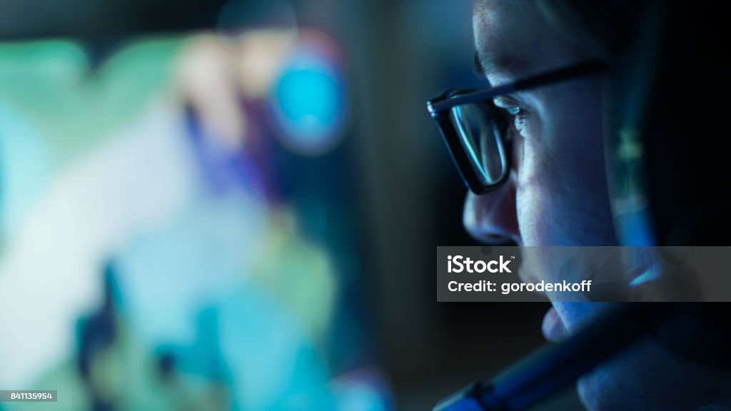 Close-up Shot of Professional Gamer Plays in MMORPG/ Strategy Video Game on His Computer. He's Participating in Online Cyber Games Tournament, Plays at Home, or in Internet Cafe. He Wears Glasses and Gaming Headsets. Computer Monitor Stock Photo