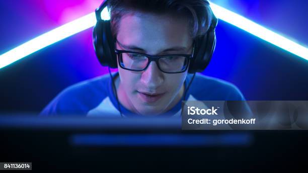 Professional Gamer Plays In Mmorpg Strategy Shooter Video Game On His Computer Hes Participating In Online Cyber Games Tournament Plays At Home Or In Internet Cafe He Wears Glasses And Gaming Headphones Talks Into Microphone Stock Photo - Download Image Now