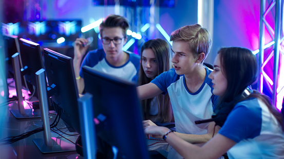 Team of Professional Boys and Girls Gamers Actively Thinking/ Discussing Game Strategy/ Tactic, They're In Internet Cafe or on Cyber Games Tournament.