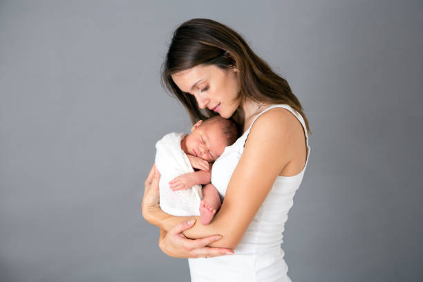 mother kissing and hugging newborn son at gray background, tender, care, love - mother baby new kissing imagens e fotografias de stock