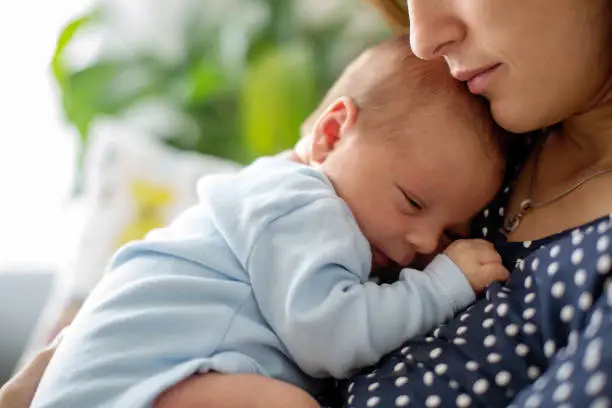 Photo of Young mother, holding tenderly her newborn baby boy