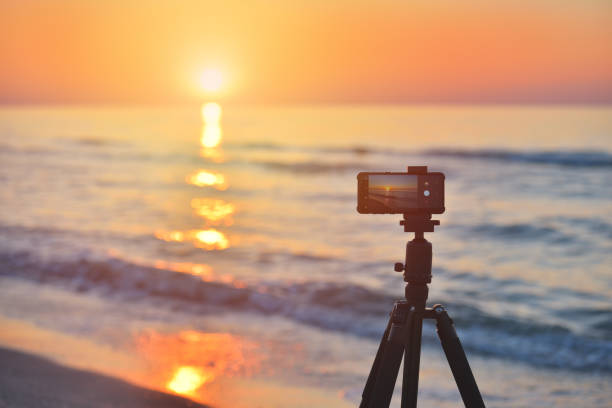 Sunrise over the sea coast. Fireball of the sun above the horizon in a colorful orange sky. Smartphone camera on a tripod in the foreground stock photo