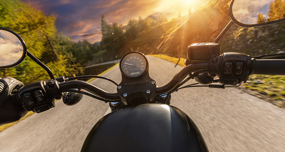 Detail of motorcycle handlebars. View from driver perspective, beautiful Alpine landscape in sunset light. Travel and sport photography in outdoor. Speed and freedom concept