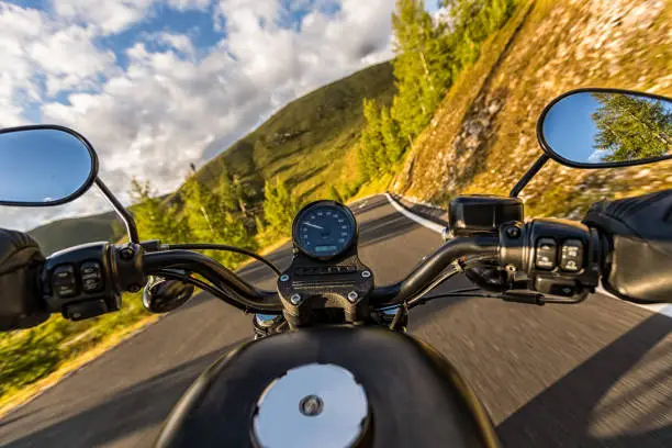 Detail of motorcycle handlebars. View from driver perspective, beautiful Alpine landscape in sunset light. Travel and sport photography in outdoor. Speed and freedom concept