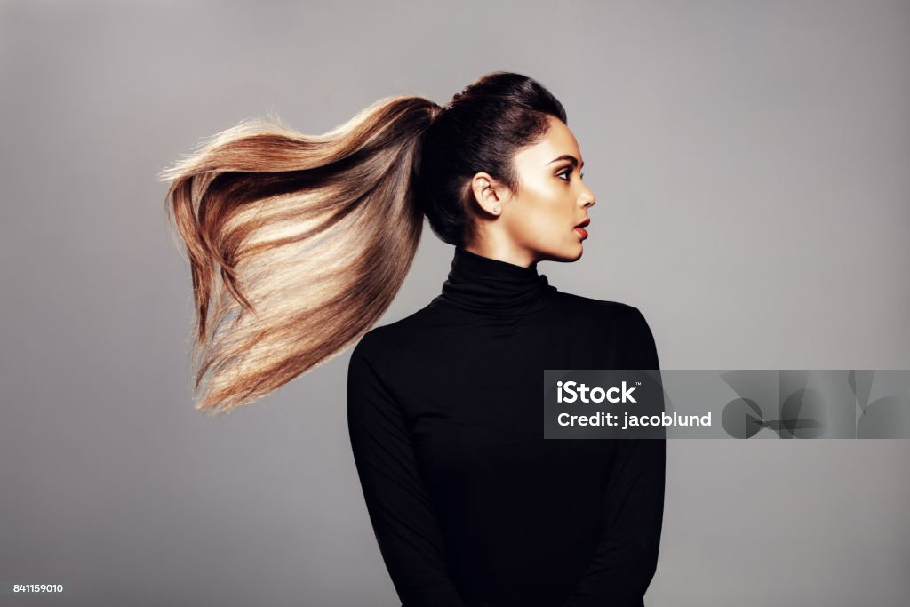 Stylish young woman with flying hair Studio shot of stylish young woman with flying hair against grey background. Female fashion model with long hair. Ponytail Stock Photo