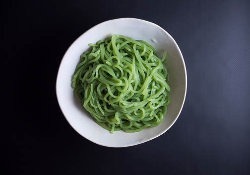 Japanese konjac noodles with spinach in rustic bowl isolated on black background
