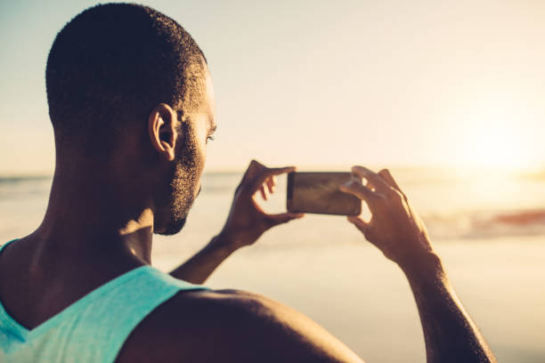 homme africain, faire de la photographie mobile sur la plage - mobilestock photos et images de collection