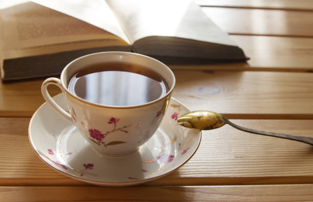 istock cup of tea and book on wooden table, lit by the sun. 841167470
