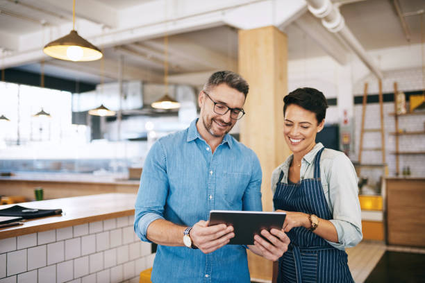 Running a coffee shop using a smart management system Shot of a man and woman using a digital tablet together in their coffee shop cafe tablet stock pictures, royalty-free photos & images
