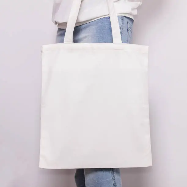 Girl in blue jeans holds blank cotton eco tote bag, design mockup. Handmade shopping bag for girls.