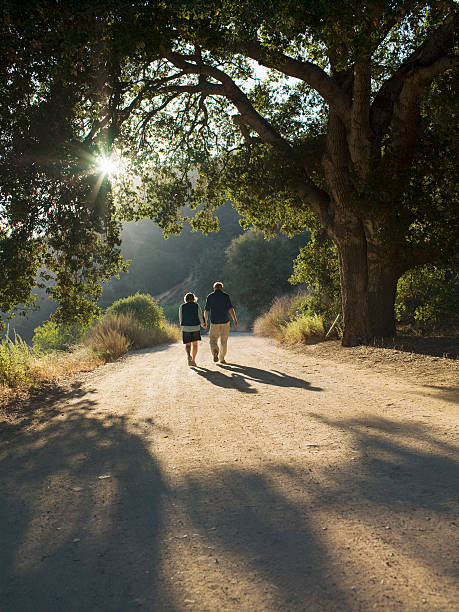 coppia matura camminare lungo strada in terra battuta - holding hands couple senior couple togetherness foto e immagini stock