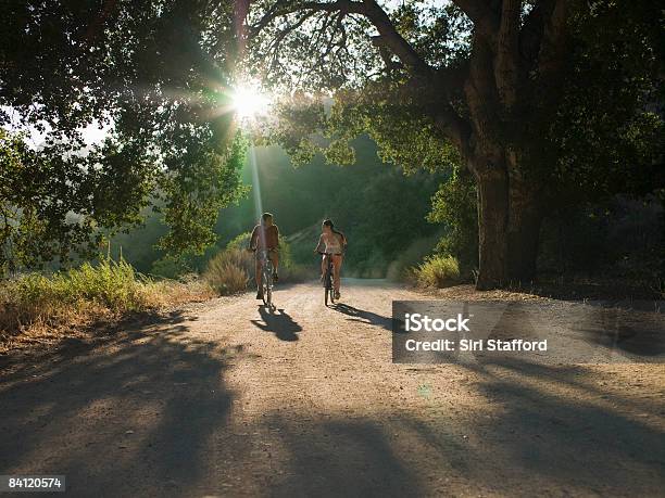 Young Couple Biking Down Dirt Road Stock Photo - Download Image Now - Cycling, Asian and Indian Ethnicities, Bicycle