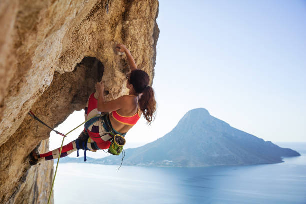 Young woman struggling to climb ledge on cliff stock photo