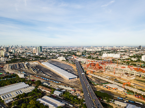 The very high aspect of new Bangkok main train station with cars traveling beside on highway. While train station is constructing on right side of highway, old trains are also parking on another side.
