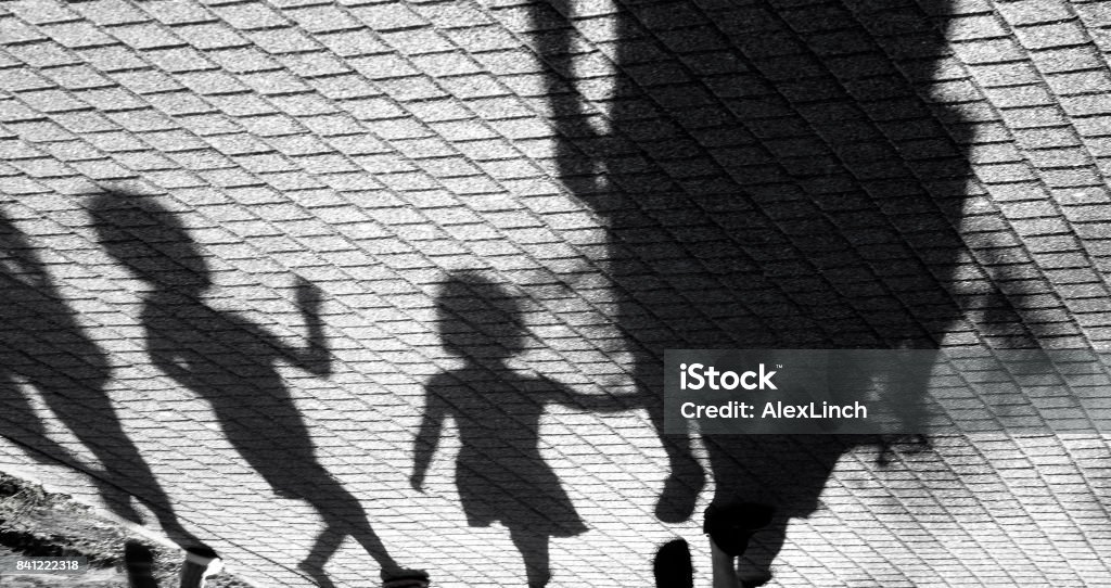 Blurry shadow of a little boy and a girl walking with adults Blurry shadow of a little boy and a girl walking with adults on park pavement in black and white Child Stock Photo