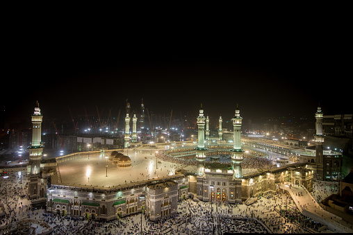 Mecca holy mosque at night with all minarets in light with people around