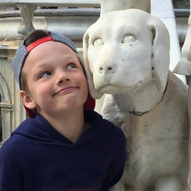 Boying mugging for the camera beside a dog statue. Palermo, Sicily.