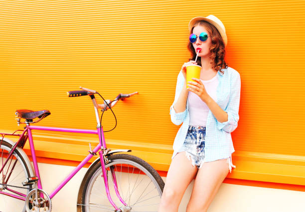 istock Summer woman drinks fruit juice from cup with retro bicycle on a colorful orange background 841233636