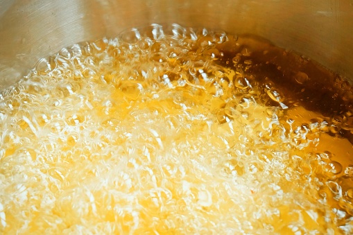 Close Up of Golden Texture of Shining Yellow Hot Oil Boiling and Creating Bubbles in A Silver Pan.