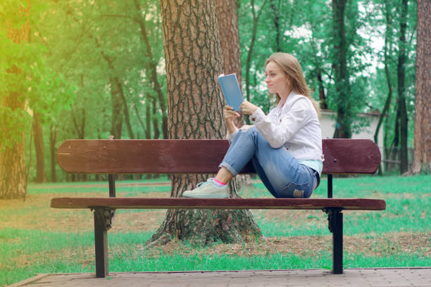 istock Beautiful young woman on a nature bench reading a book 841245656