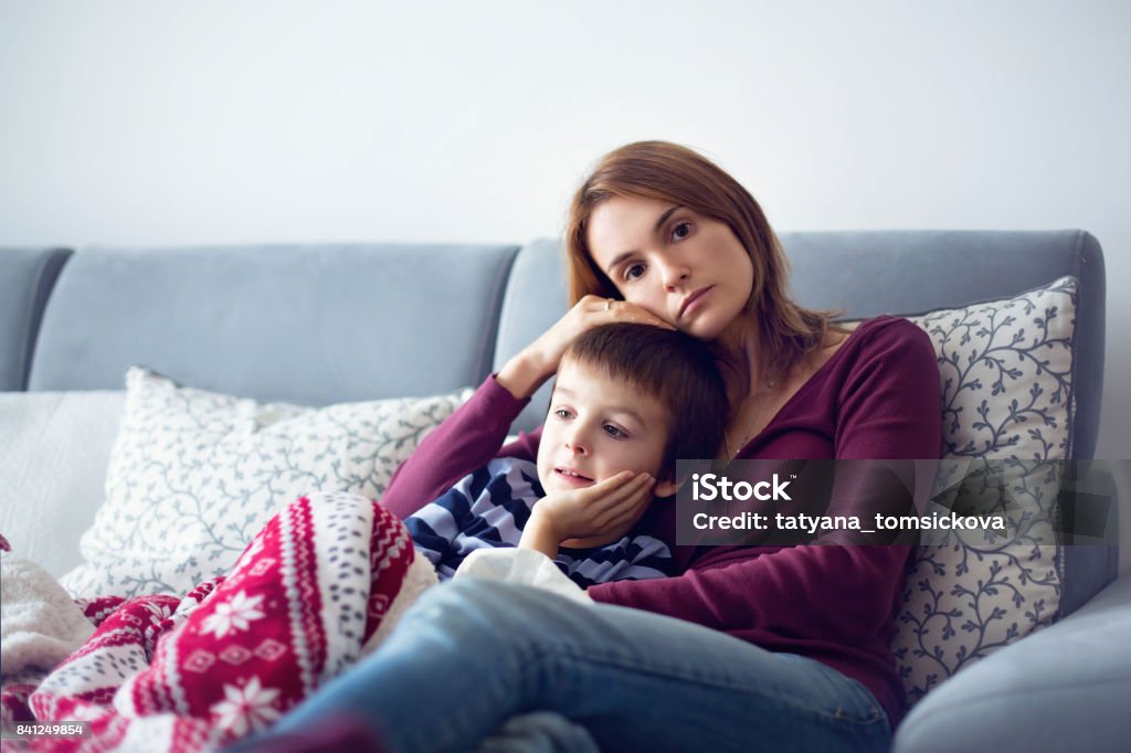 Young mother, holding her little sick boy Young mother, holding her little sick boy, lying together on the couch Mother Stock Photo