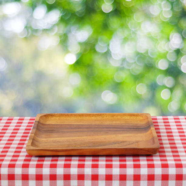 istock Empty wooden tray on table with red tablecloth over blur trees with bokeh background, for food and product display montage 841253280