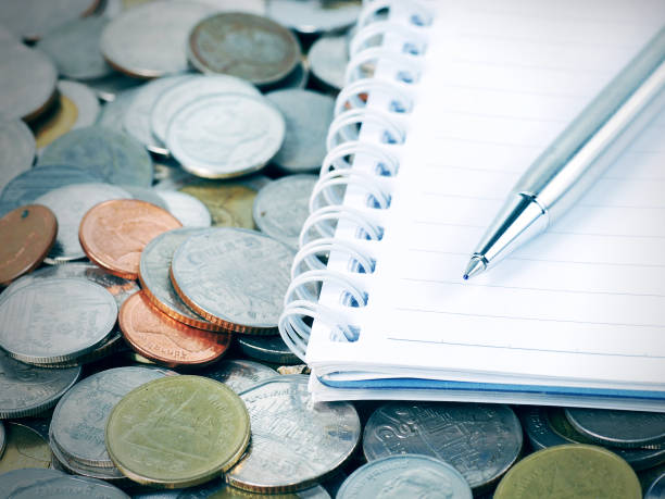 silver pen on notebook with coins background in cool tone color