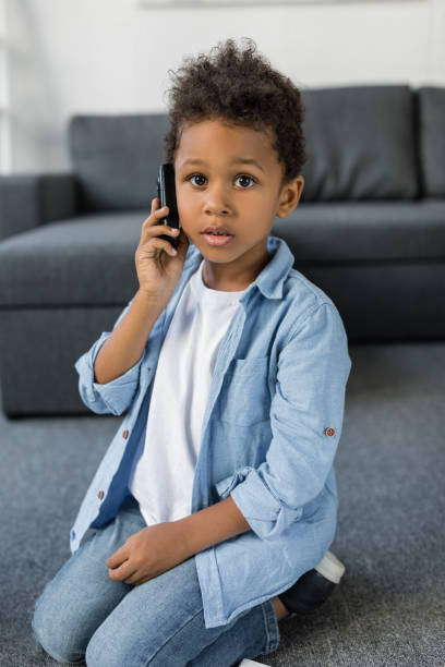 istock cute afro boy talking by phone while sitting on floor on living room 841268860