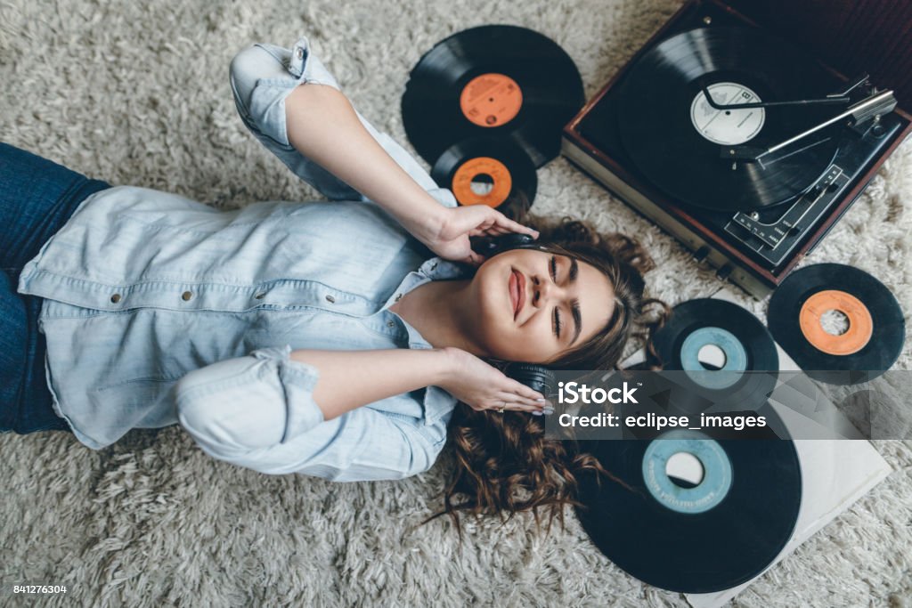 Young woman enjoing music from gramophone Young retro woman listening music on floor Record - Analog Audio Stock Photo