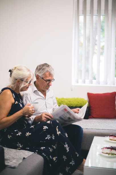 istock Senior Couple Relaxing On Sofa At Home Reading Newspaper 841281880