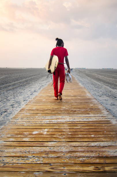 Young man walking towards seaside with surfboard