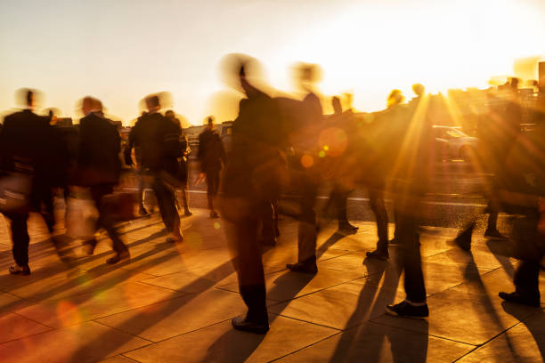 Crowd of business people at sunset, London, England Crowd of motion blurred business people rushing in sunset light. Many shadows on walkway are visible as well as sunrays between walking commuters. A lot of intentional lens flares can be seen. Back lit, orange and bronze colors,  50 megapixel image, London Bridge, City of London, United Kingdom unidentifiable persons stock pictures, royalty-free photos & images
