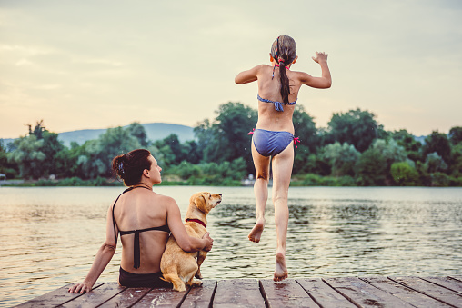 Mother and dog sitting on a dock and looking at daughter jumping into water