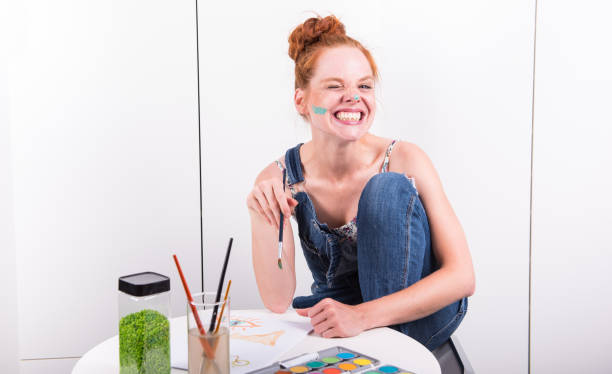 attractive redhead is making fun during painting with water colours at home